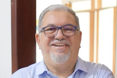 foto do vice-prefeito. Tem pele de cor branca, está usando blusa azul claro, tem barba e cabelos brancos e usa óculos de armação azul