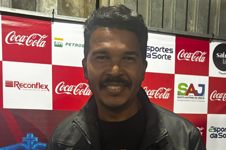 Foto do artista Jhow Show usando jaqueta de couro preta, ao fundo propaganda da coca-cola