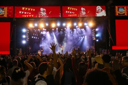 Na foto há uma multidão assistindo a um show, no fundo há o palco principal do evento